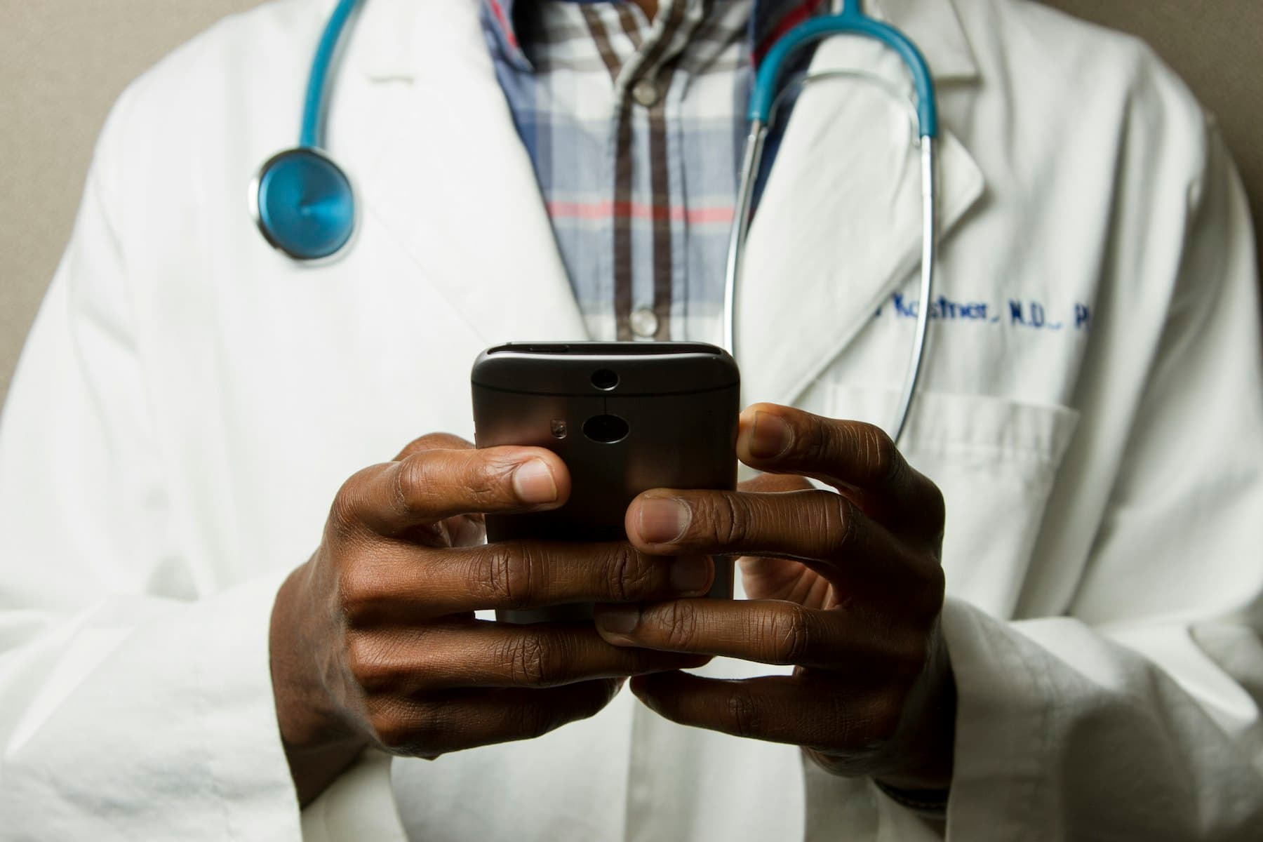 A doctor in a white coat typing on a phone